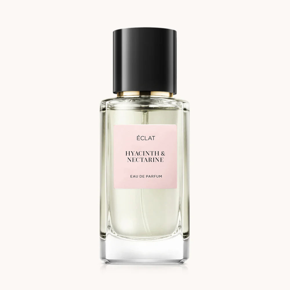 Flacon of the women’s perfume dupe ÉCLAT Hyacinth & Nectarine, an elegant transparent glass bottle with a black cylindrical magnetic cap and a light pink label. The label displays the brand name ÉCLAT, the name Hyacinth & Nectarine, and the phrase “Eau de Parfum”.