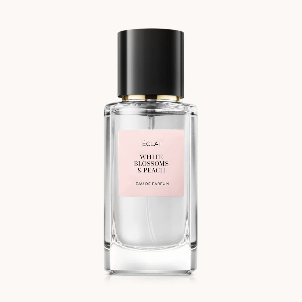 Flacon of the women’s perfume dupe ÉCLAT White Blossoms & Peach, an elegant transparent glass bottle with a black cylindrical magnetic cap and a light pink label. The label displays the brand name ÉCLAT, the name White Blossoms & Peach, and the phrase “Eau de Parfum”.