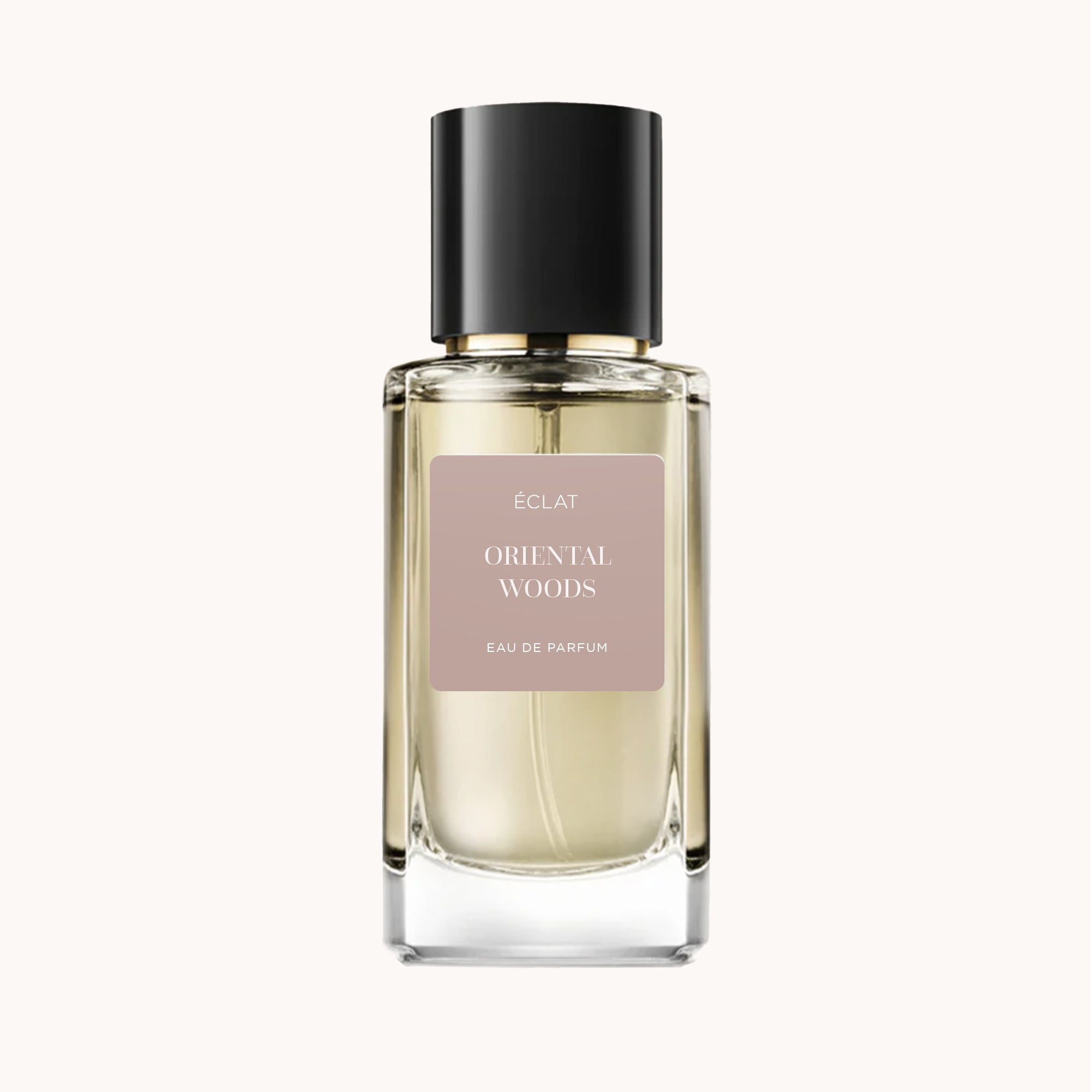 Perfumy ÉCLAT Oriental Woods w przezroczystej szklanej butelce o fasetowanej powierzchni, z błyszczącą czarną nakrętką i miękką beżową etykietą.