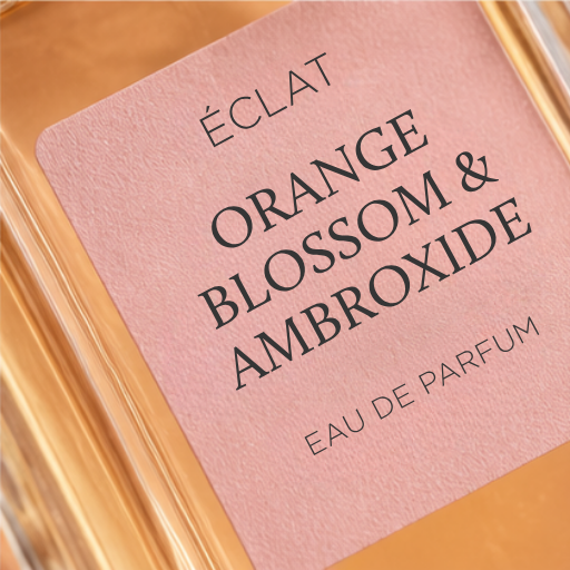 Fasetowany flakon ze szkła z różową etykietą pokazującą nazwę ÉCLAT Orange Blossom & Ambroxide.