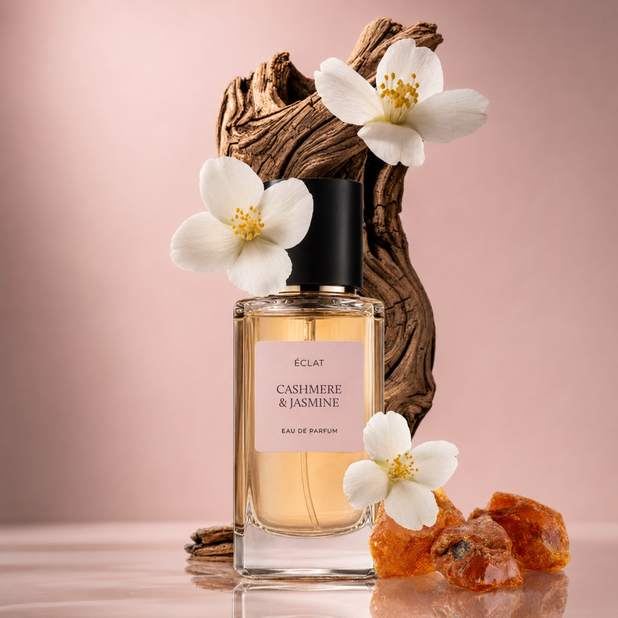 Przezroczysty szklany flakon perfum ÉCLAT Cashmere & Jasmine z czarną nakrętką, otoczony białymi kwiatami jaśminu i bursztynowymi kamieniami na drewnianym tle.