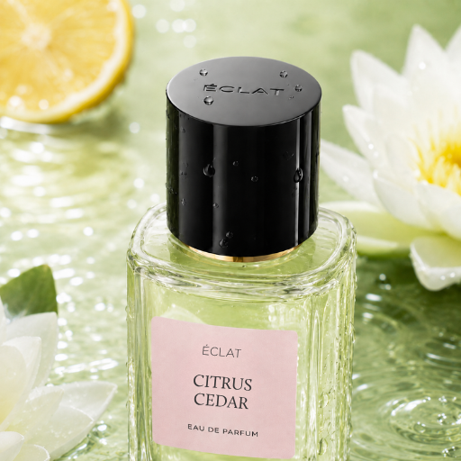 Fasetowana szklana butelka ÉCLAT Citrus Cedar z czarną nakrętką na powierzchni wody z plasterkiem cytryny i białymi kwiatami.
