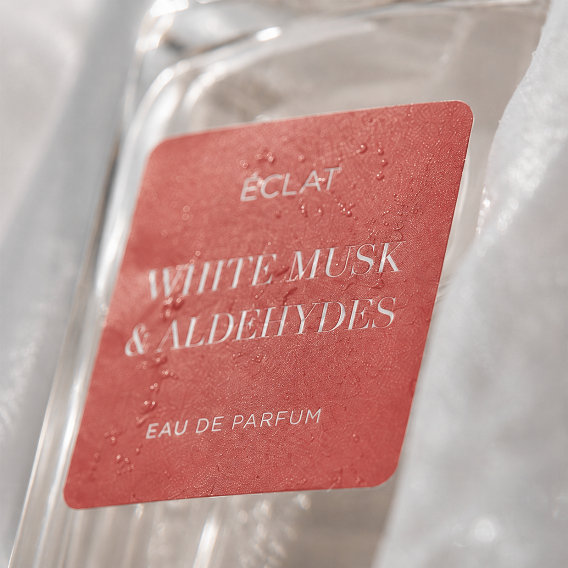 Zbliżenie butelki perfum ÉCLAT White Musk & Aldehydes z czerwonym teksturowanym etykietą.