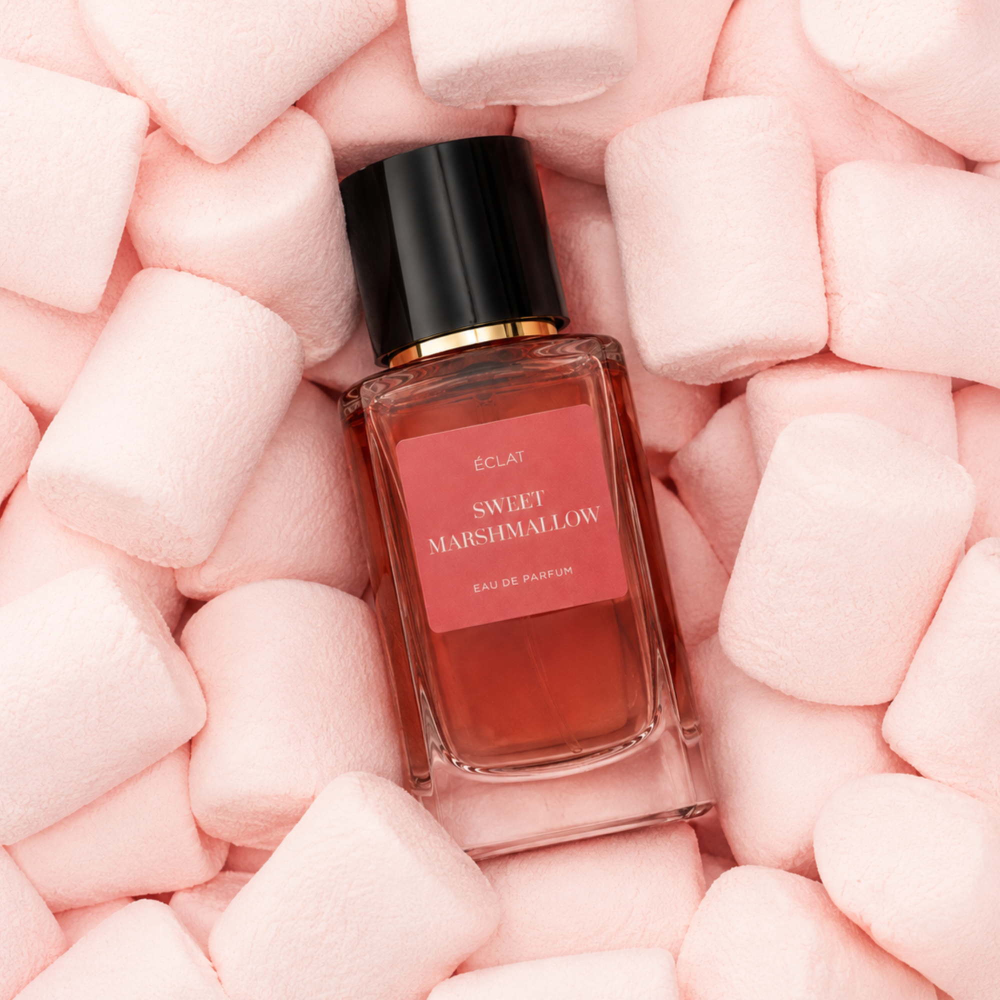 Szklana butelka ÉCLAT Sweet Marshmallow otoczona miękkimi różowymi piankami, z czarną zakrętką i różową etykietą.