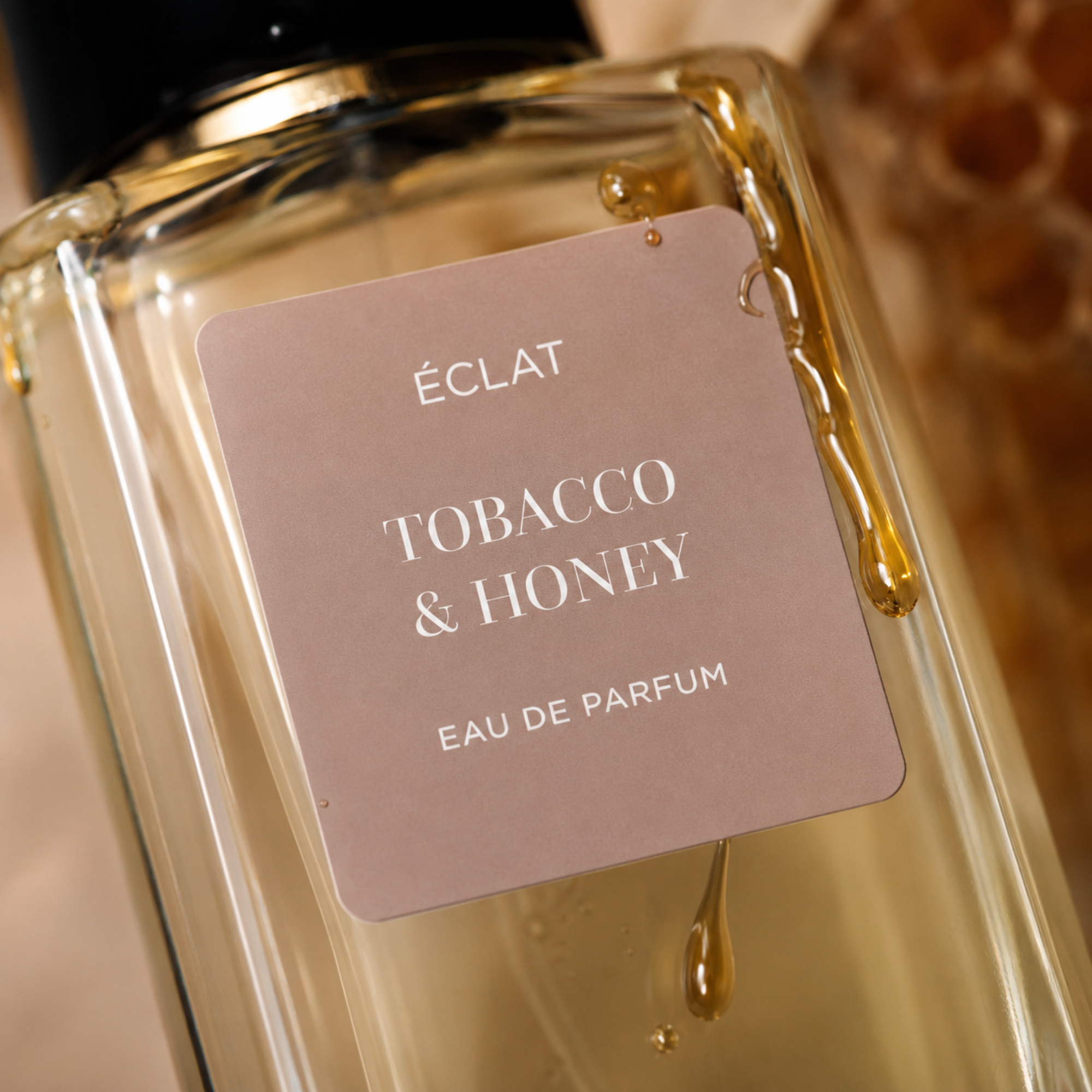 Flakon perfum ÉCLAT Tobacco & Honey z jasnobrązową matową etykietą i kroplą miodu spływającą po powierzchni szkła.