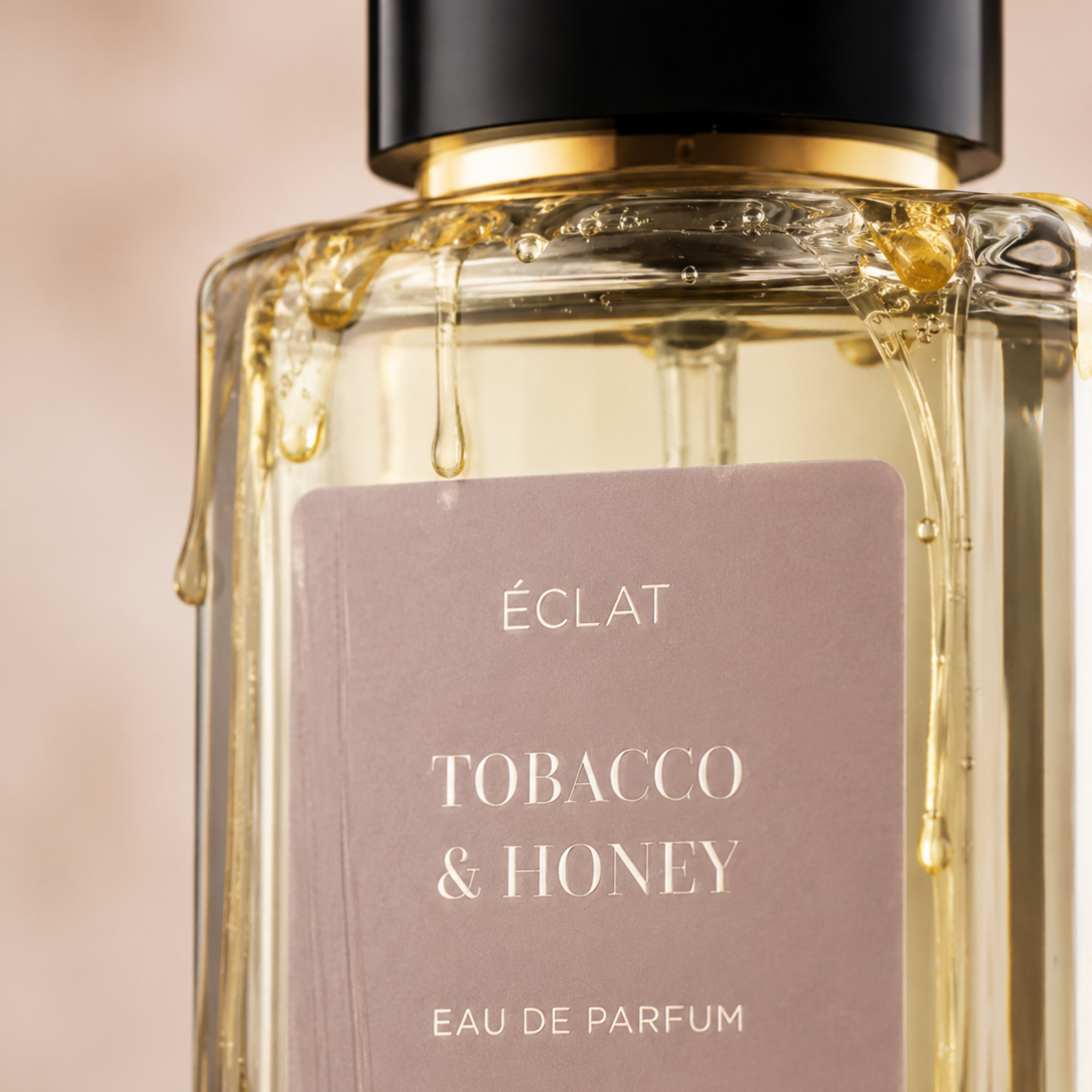Fasetowana szklana butelka ÉCLAT Tobacco & Honey z satynową etykietą i czarnym korkiem, ozdobiona kroplami miodu.