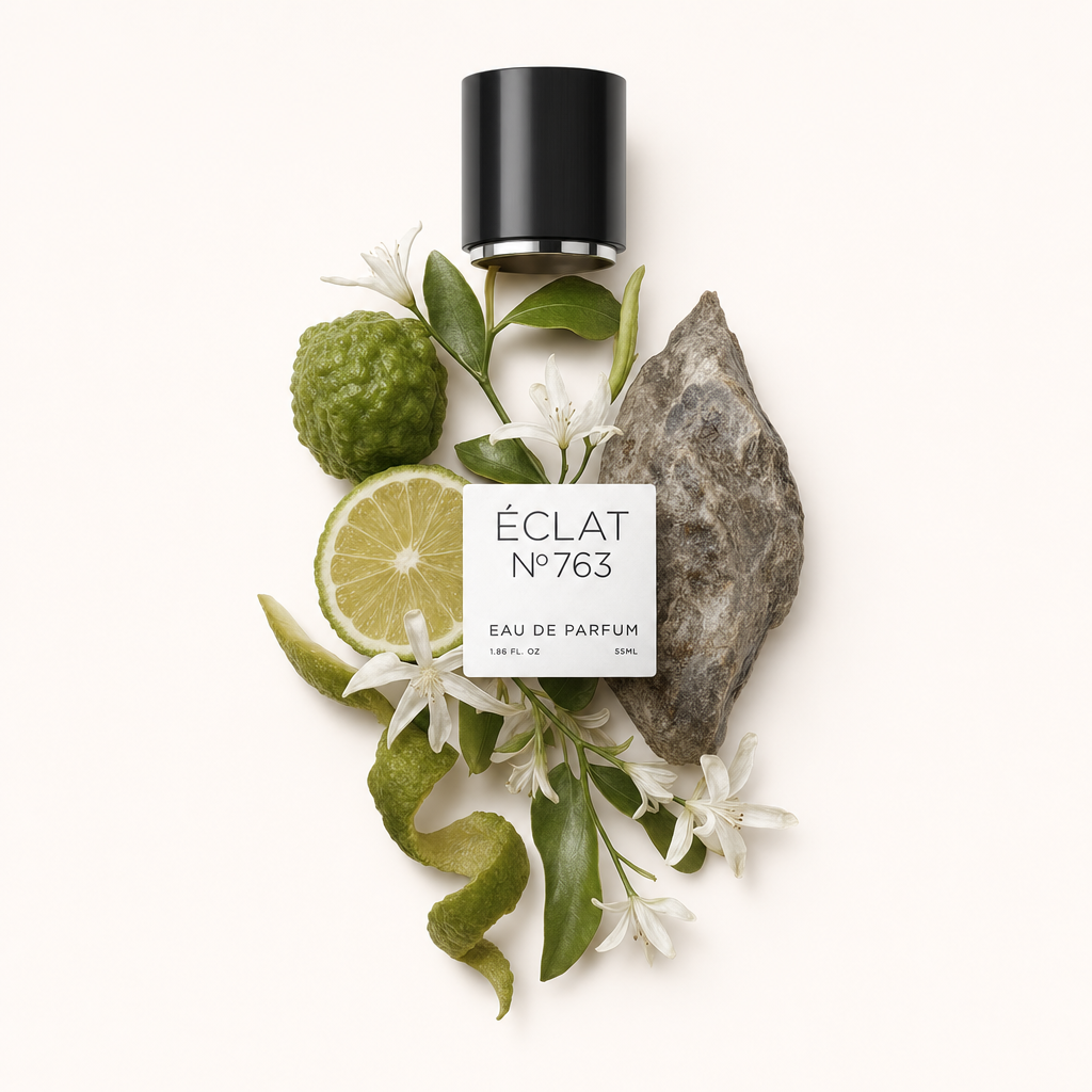Kompozycja z bergamotki, plasterków limonki, zielonych liści i małych białych kwiatów otacza czarną nasadkę z etykietą ÉCLAT Ambergris & Bergamot.
