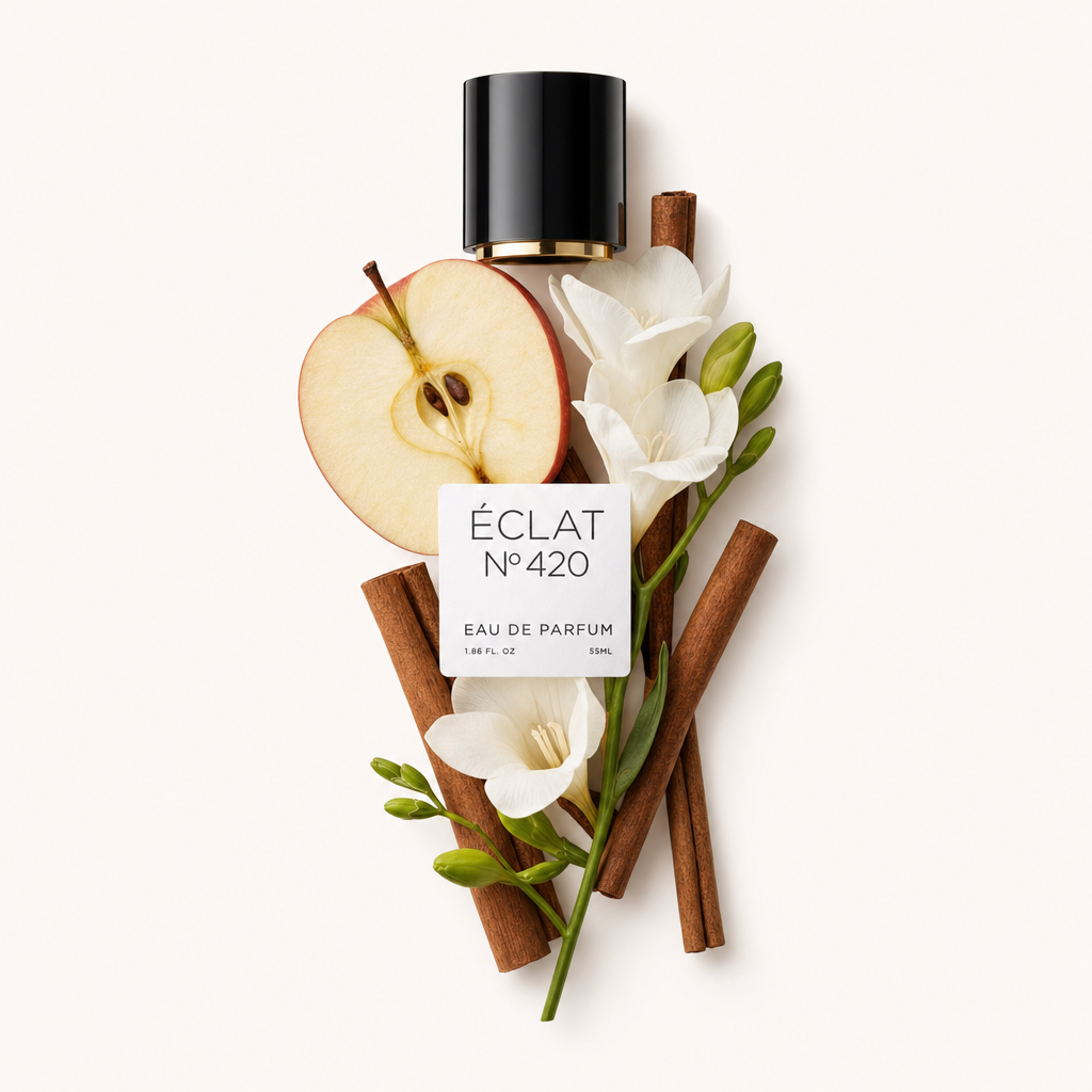 Starannie ułożona martwa natura z plastrami jabłka, laskami cynamonu i białymi kwiatami wokół czarnej nakrętki z etykietą ÉCLAT Apple & Cinnamon.