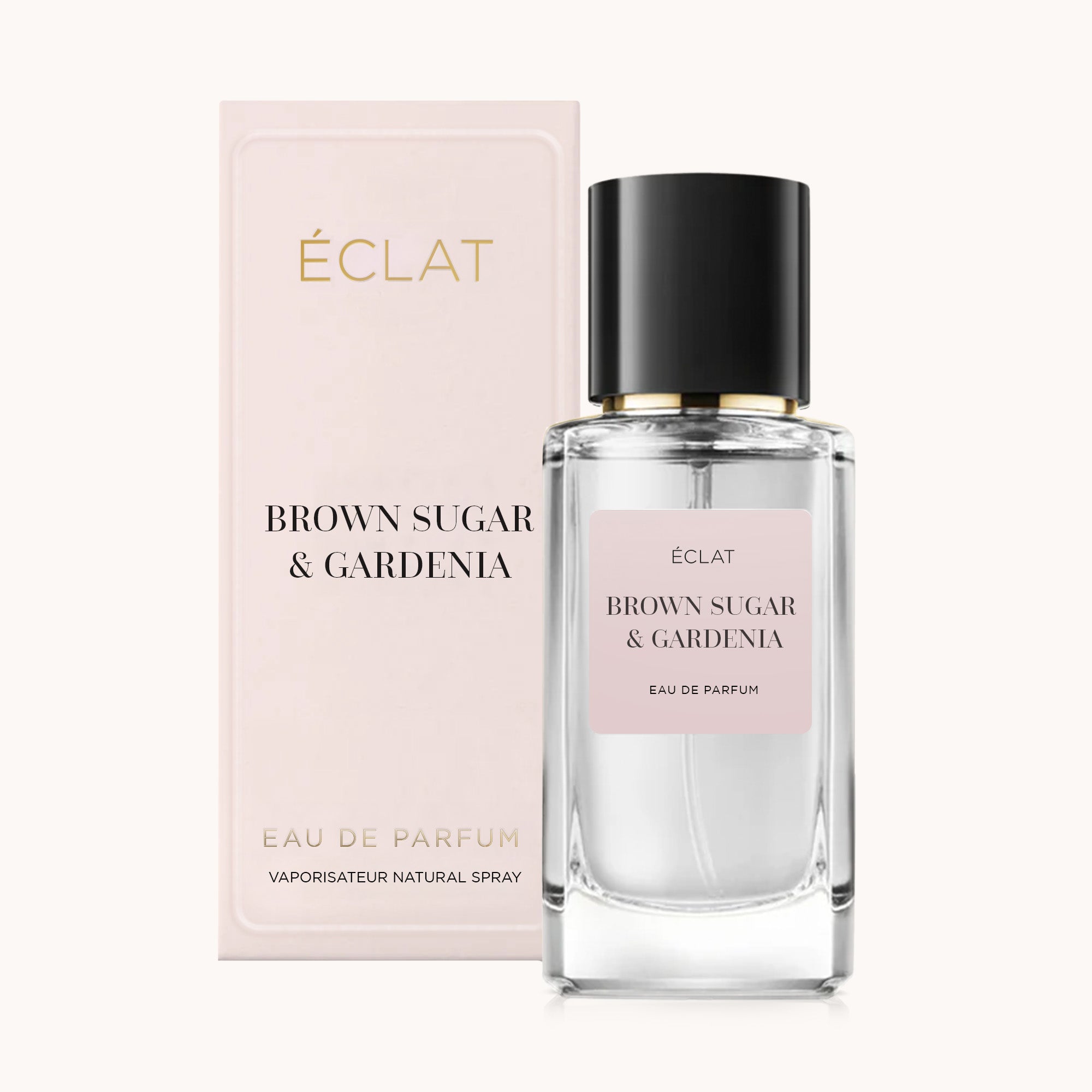 Fasadowana szklana butelka perfum ÉCLAT Brown Sugar & Gardenia z czarną nakrętką, obok miękkiego różowego pudełka prezentacyjnego.