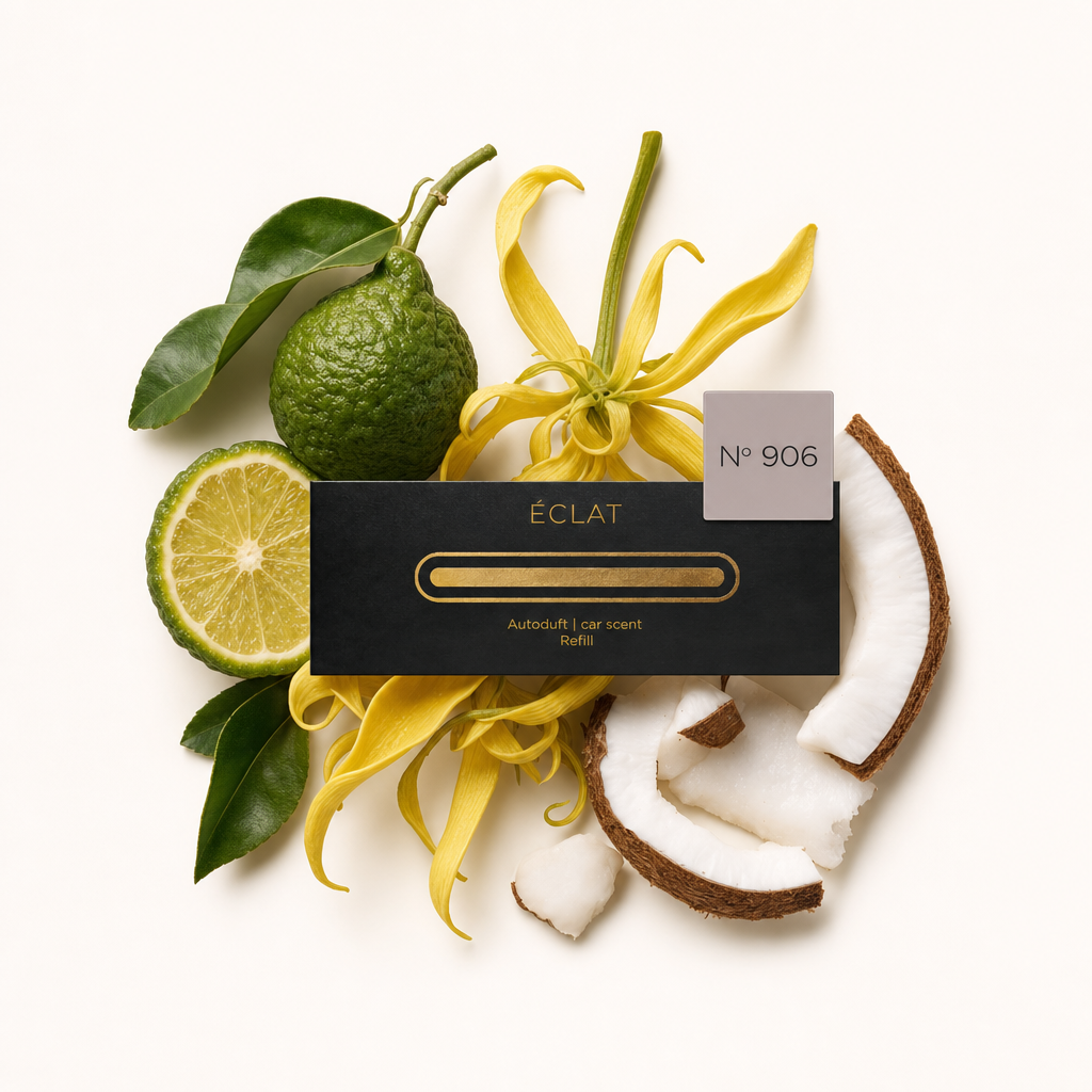 Aranżacja z bergamotki, kwiatów ylang-ylang i kawałków kokosa otacza czarną nasadkę zapachu samochodowego ÉCLAT z etykietą.