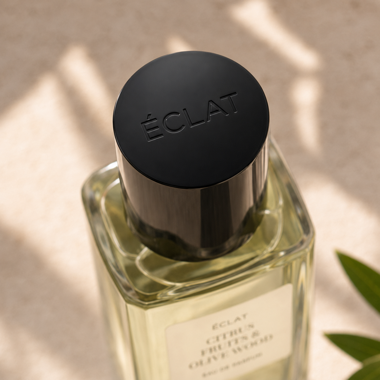 Fasetonowana szklana butelka ÉCLAT Citrus Fruits & Olive Wood z eleganckim czarnym korkiem na miękkim tle.