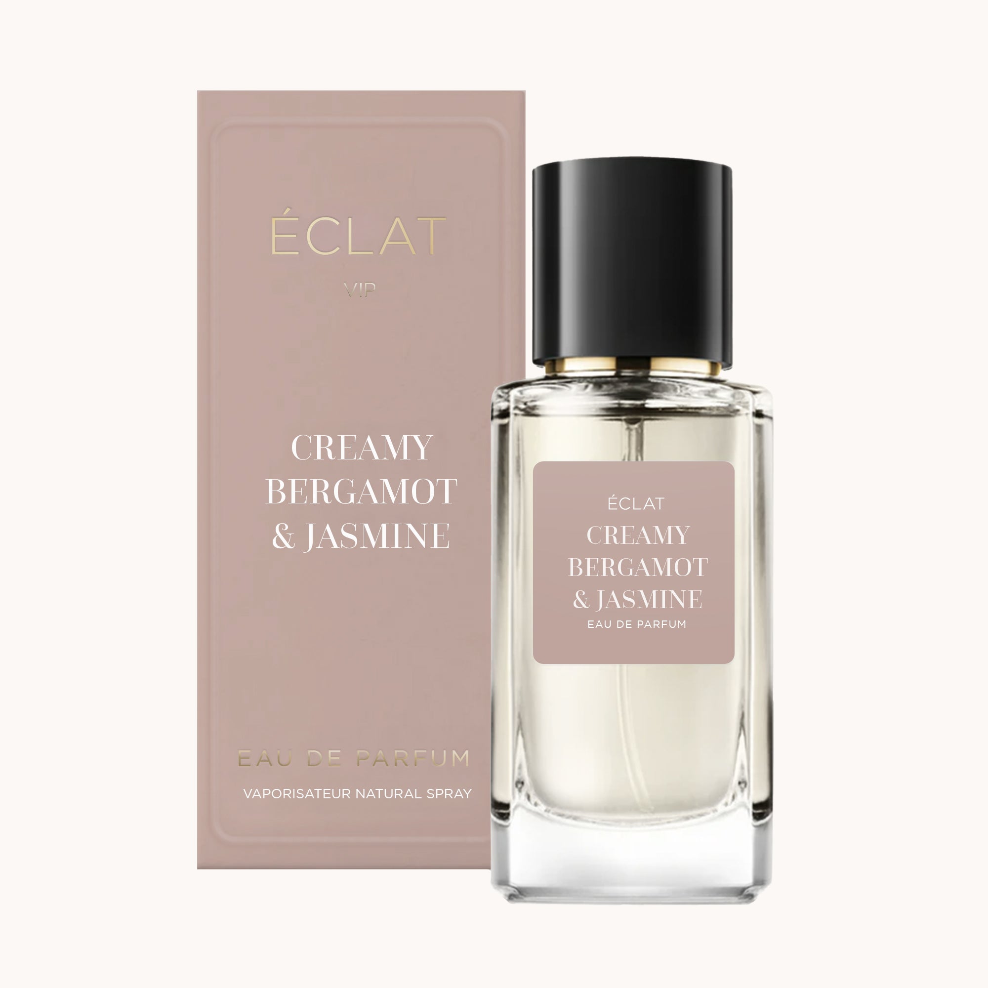 Flakon perfum ÉCLAT Creamy Bergamot & Jasmine z przezroczystym, fasetowanym designem i czarną nakrętką, obok pasującego różowego pudełka.