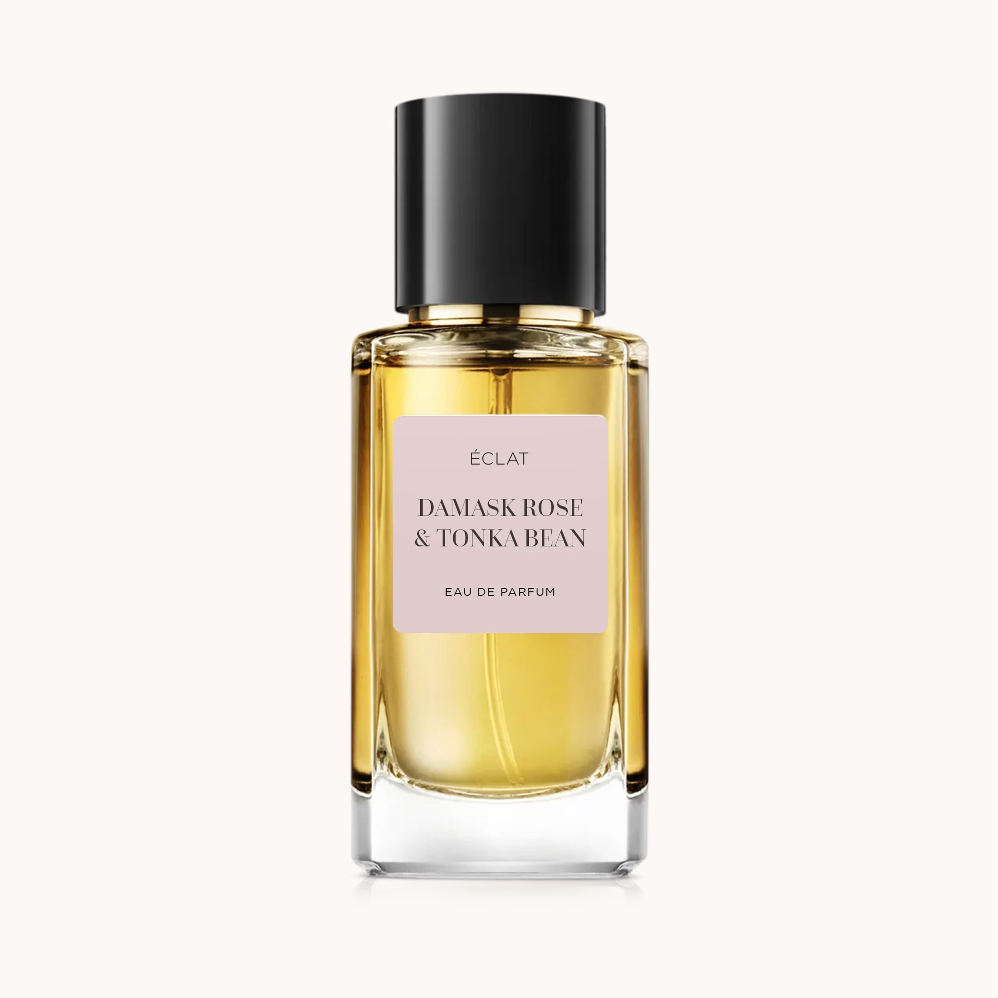 Fasadowana szklana butelka o złotym odcieniu z matową czarną nakrętką, z różową etykietą ÉCLAT Damask Rose & Tonka Bean.