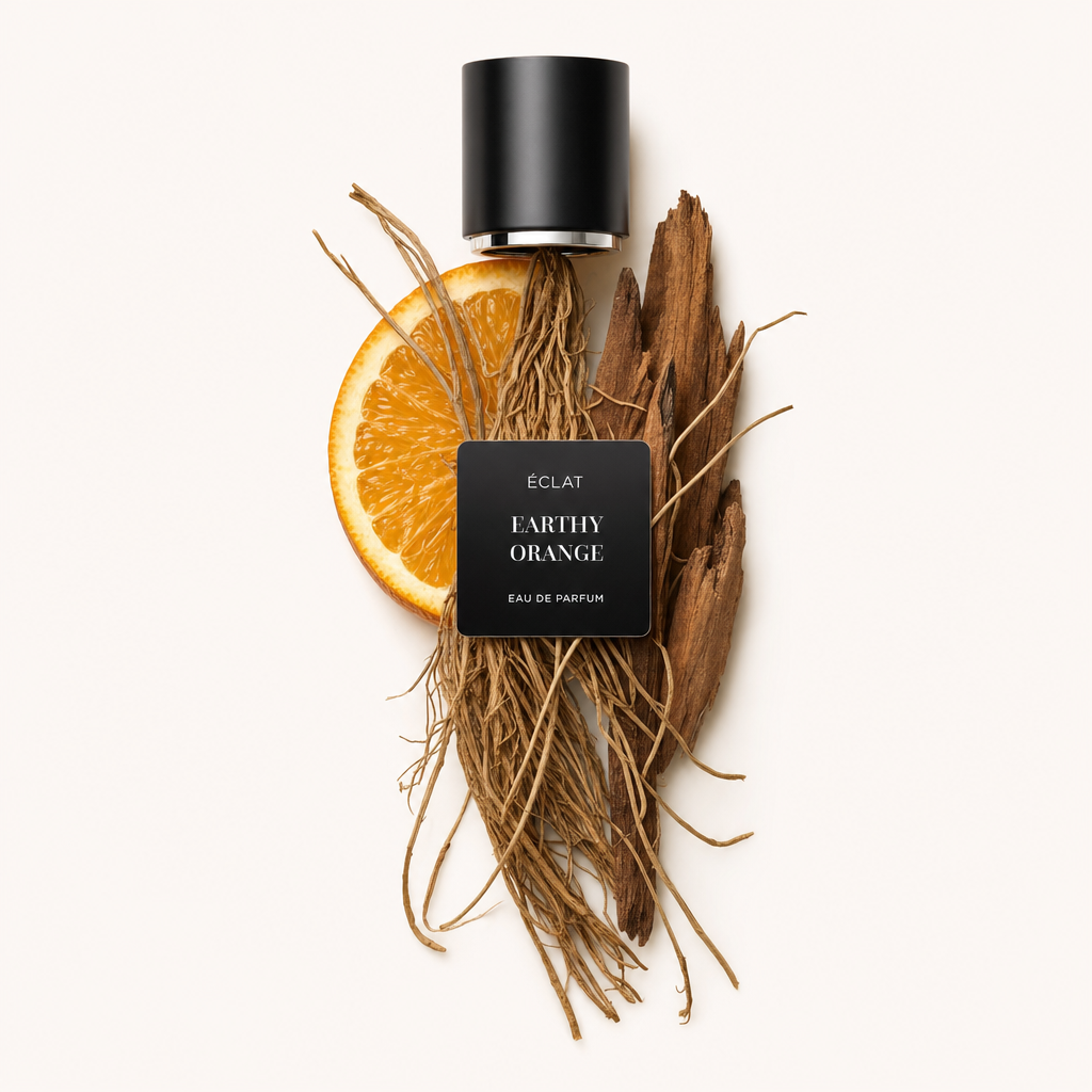 Kompozycja z ziemistych korzeni, plastra pomarańczy i kawałków drewna pod czarną nakrętką z etykietą ÉCLAT Earthy Orange.
