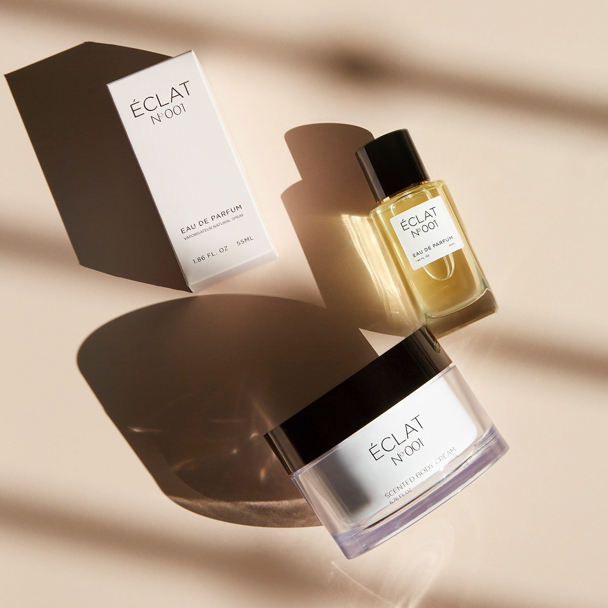 Perfumy ÉCLAT Floral Aldehydes oraz krem do ciała z czarną nakrętką obok białego pudełka na jasnej powierzchni.