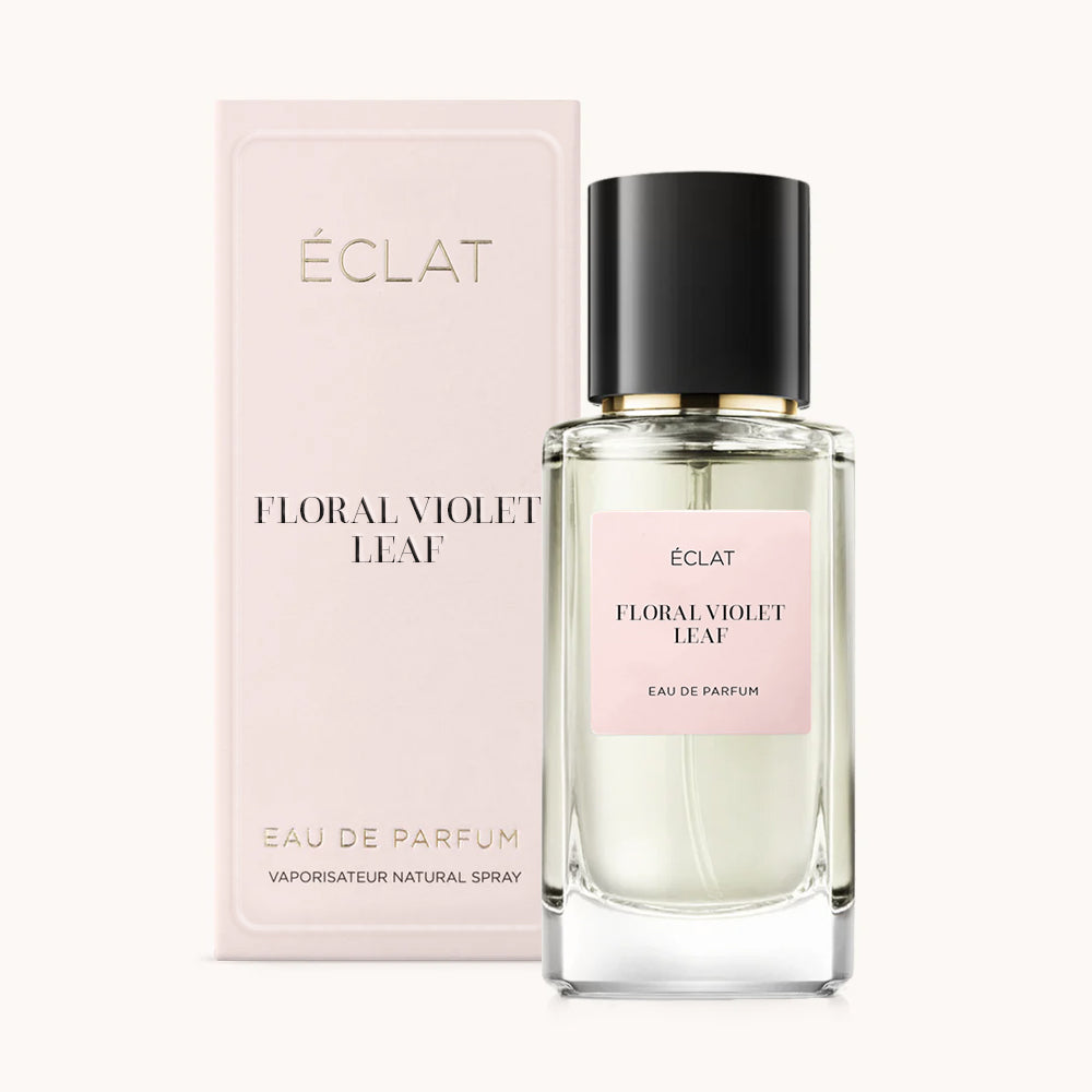 Flakon perfum ÉCLAT Floral Violet Leaf z czarną nakrętką i różową etykietą, obok dopasowanego różowego pudełka.