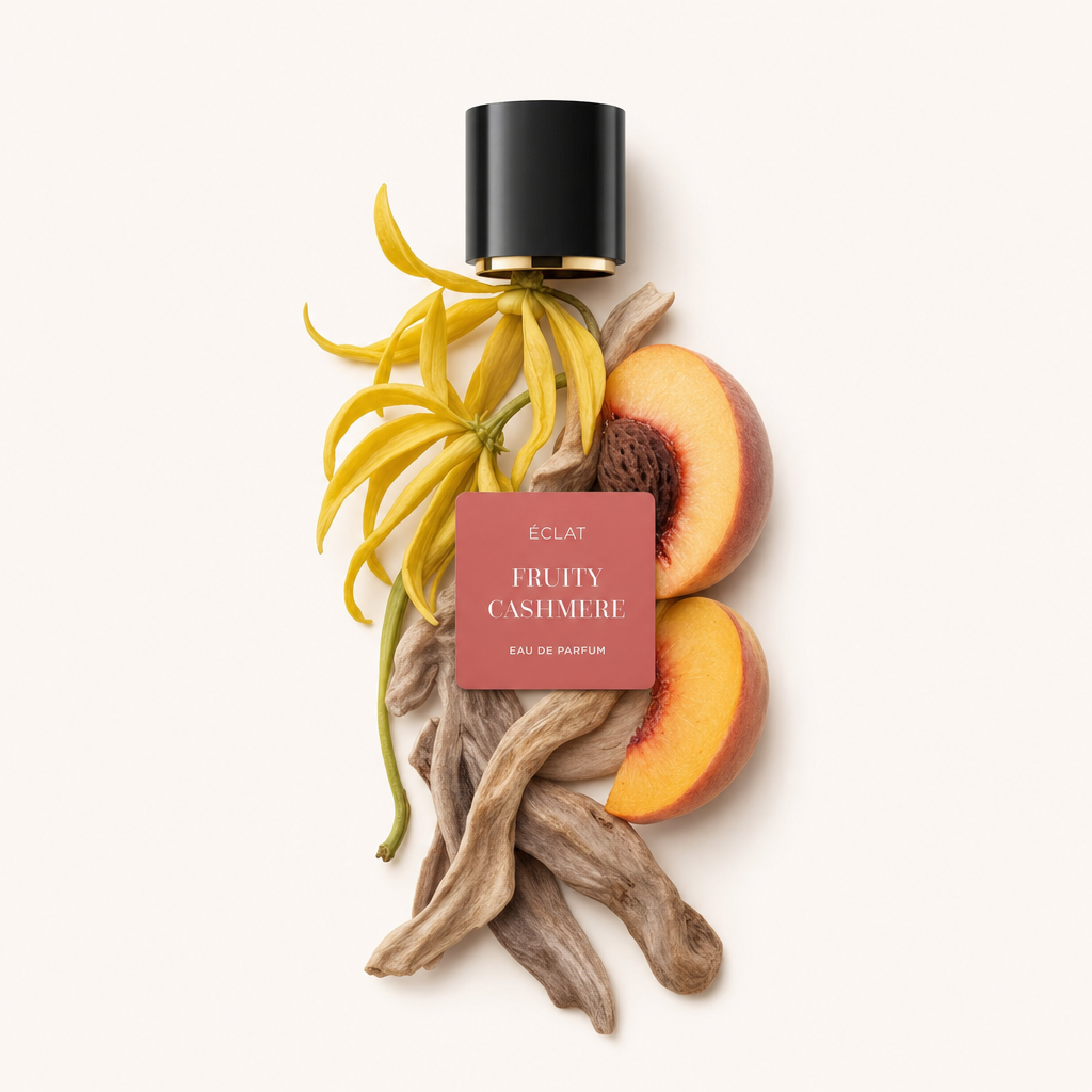 Aranżacja z kwiatów ylang-ylang, połówek brzoskwiń i patyczków sandałowych z czarną zakrętką i etykietą ÉCLAT Fruity Cashmere.