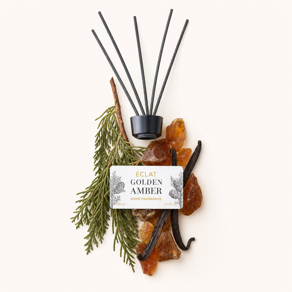 Starannie ułożona martwa natura z gałązkami cedrowymi, bursztynowymi kamieniami i laskami wanilii otaczającymi czarną nakrętkę z etykietą ÉCLAT Golden Amber.
