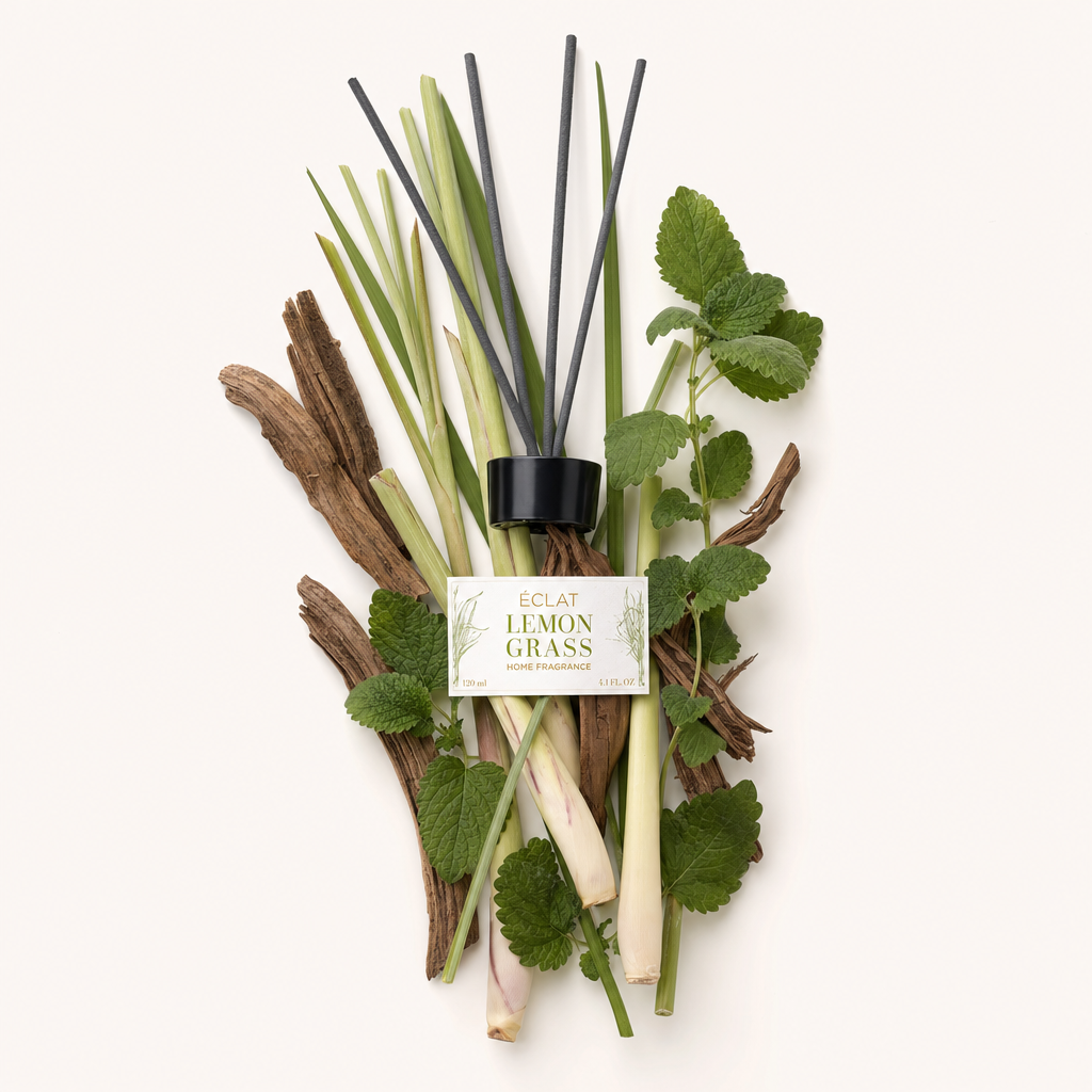 Aranżacja z trawy cytrynowej, liści mięty i kawałków drewna otacza czarną nakrętkę z etykietą ÉCLAT Lemongrass Room Fragrance Sticks.