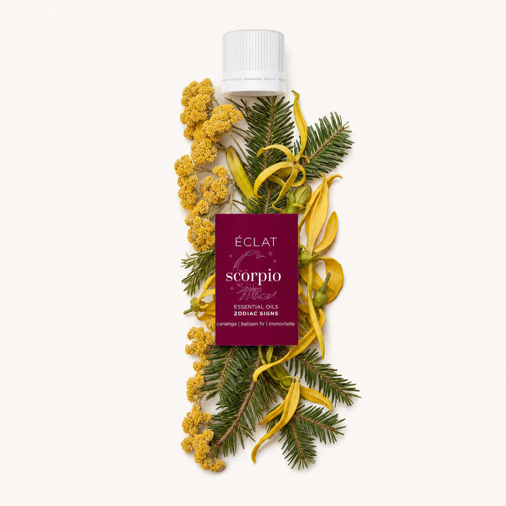 Kompozycja z żółtych kwiatów ylang-ylang, żółtych kwiatów nieśmiertelnika i zielonych gałązek jodły otacza czarną nakrętkę z etykietą olejków eterycznych Scorpio Zodiac Sign od ÉCLAT.