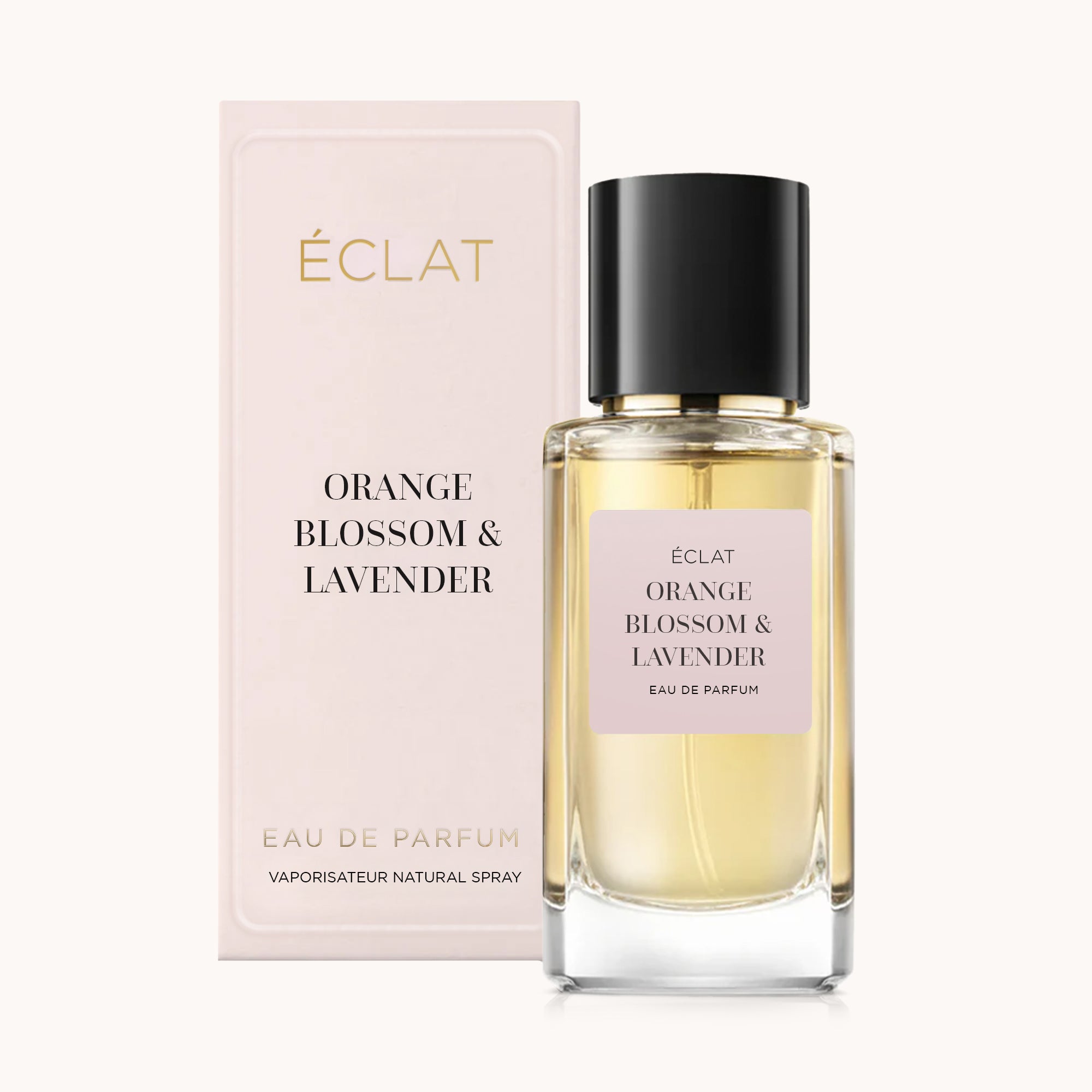 Fasetowana szklana butelka ÉCLAT Orange Blossom & Lavender z czarną nakrętką i różową etykietą, obok pasującego różowego pudełka.