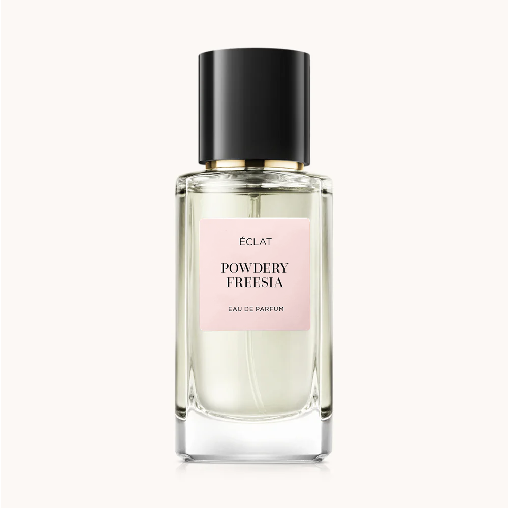 Fasetowany szklany flakon ÉCLAT Powdery Freesia z czarną zakrętką i bladoróżową etykietą.