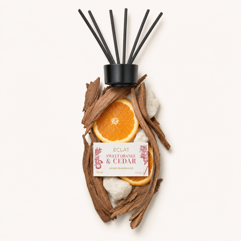 Kompozycja kawałków drewna cedrowego i plasterków słodkiej pomarańczy otacza czarną nakrętkę z etykietą ÉCLAT Sweet Orange & Cedar Room Fragrance Sticks.
