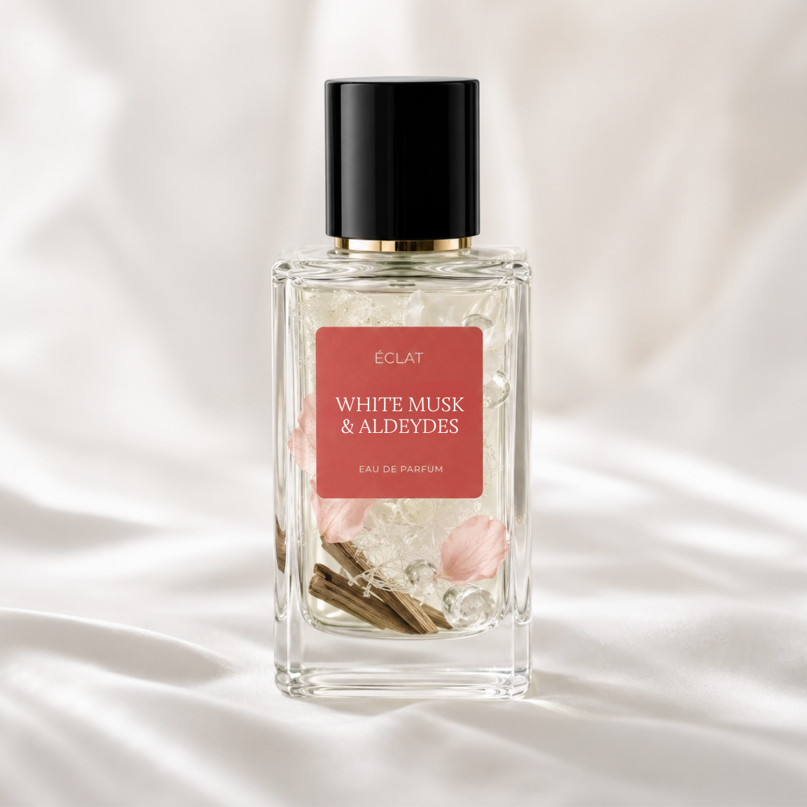 ÉCLAT White Musk & Aldehydes w szklanej, fasetowanej butelce z czarną zakrętką i czerwoną etykietą na miękkim, białym tle z tkaniny.